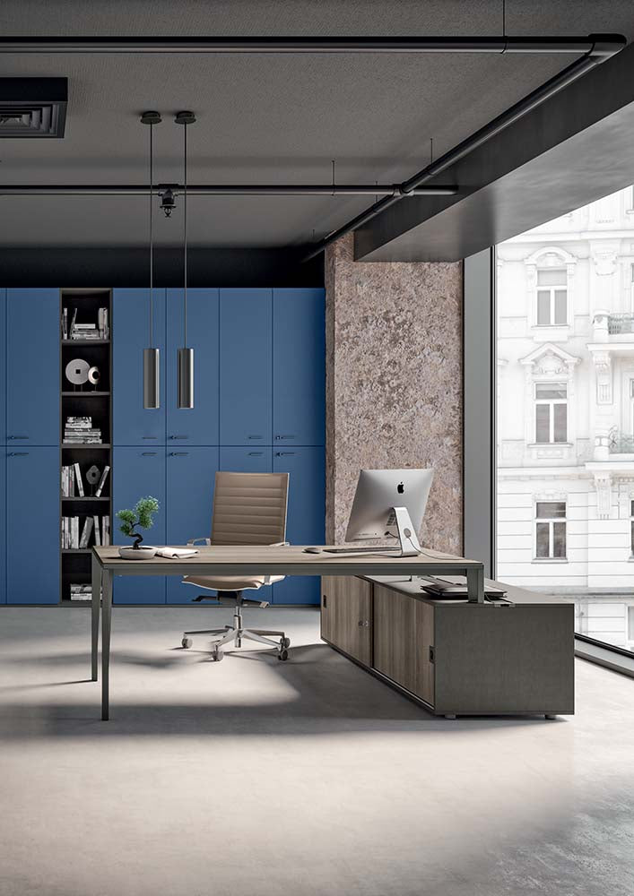 Werkplek met bureau en verlaagd aanbouwblad in donker decor, voor een blauwe kastenwand