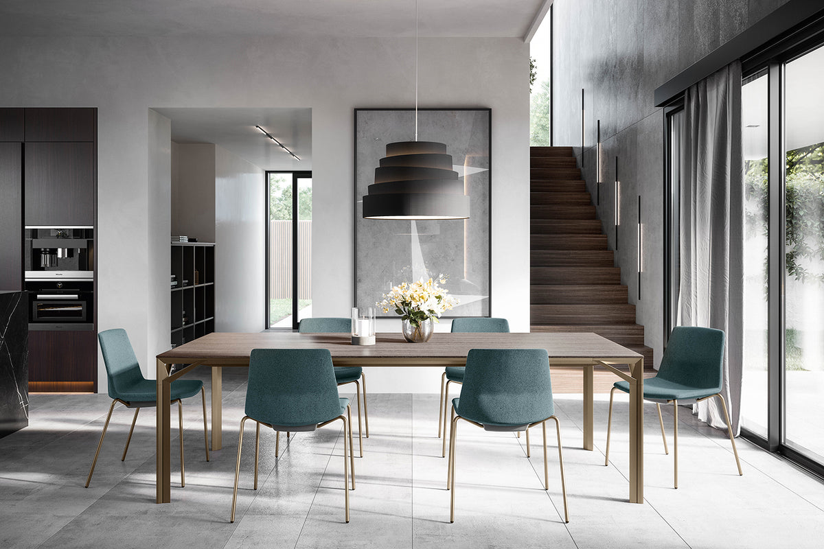 Sfeerbeeld van een eetkamer met petrolblauwe stoelen op slanke gouden poten rond een houten tafel
