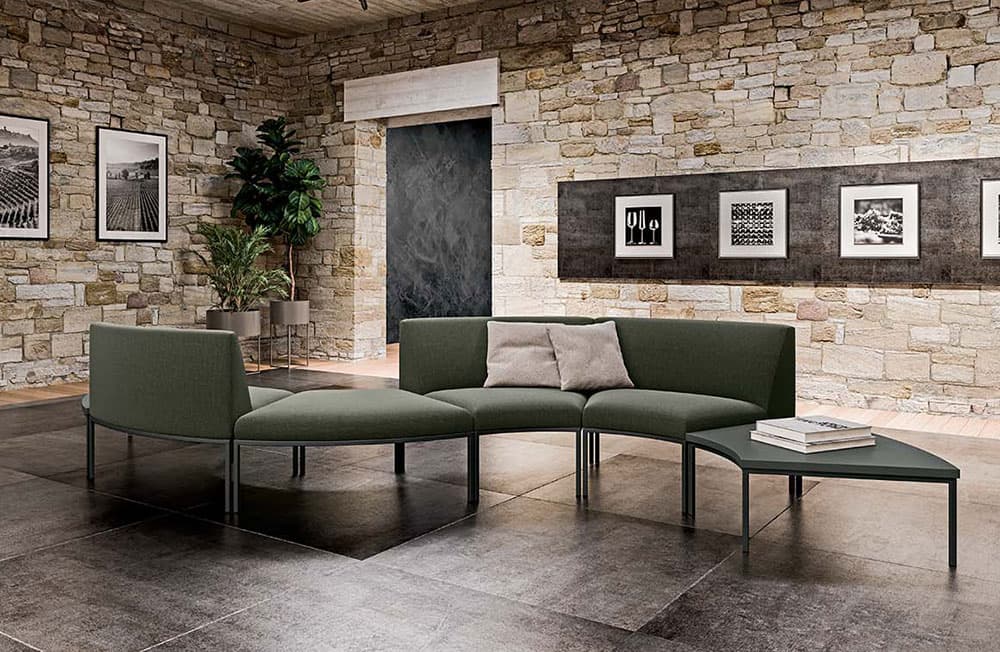 Loungehoek met groene modulaire banken en lage ronde tafels tegen een bakstenen muur