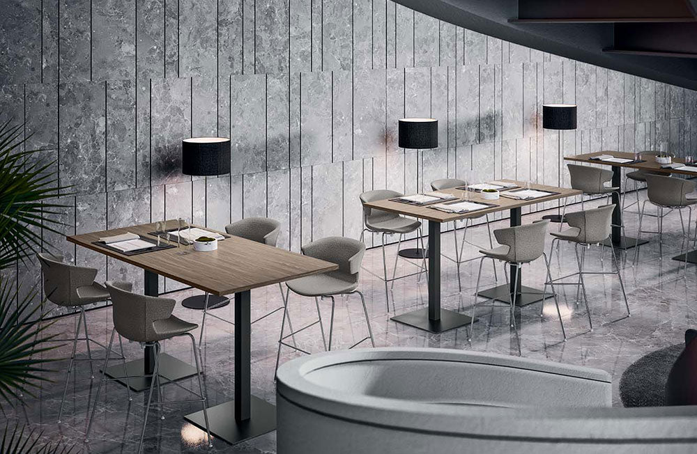 Sfeerbeeld van meerdere tafels met houten blad op zwarte kolompoten en grijze stoelen in een kantine