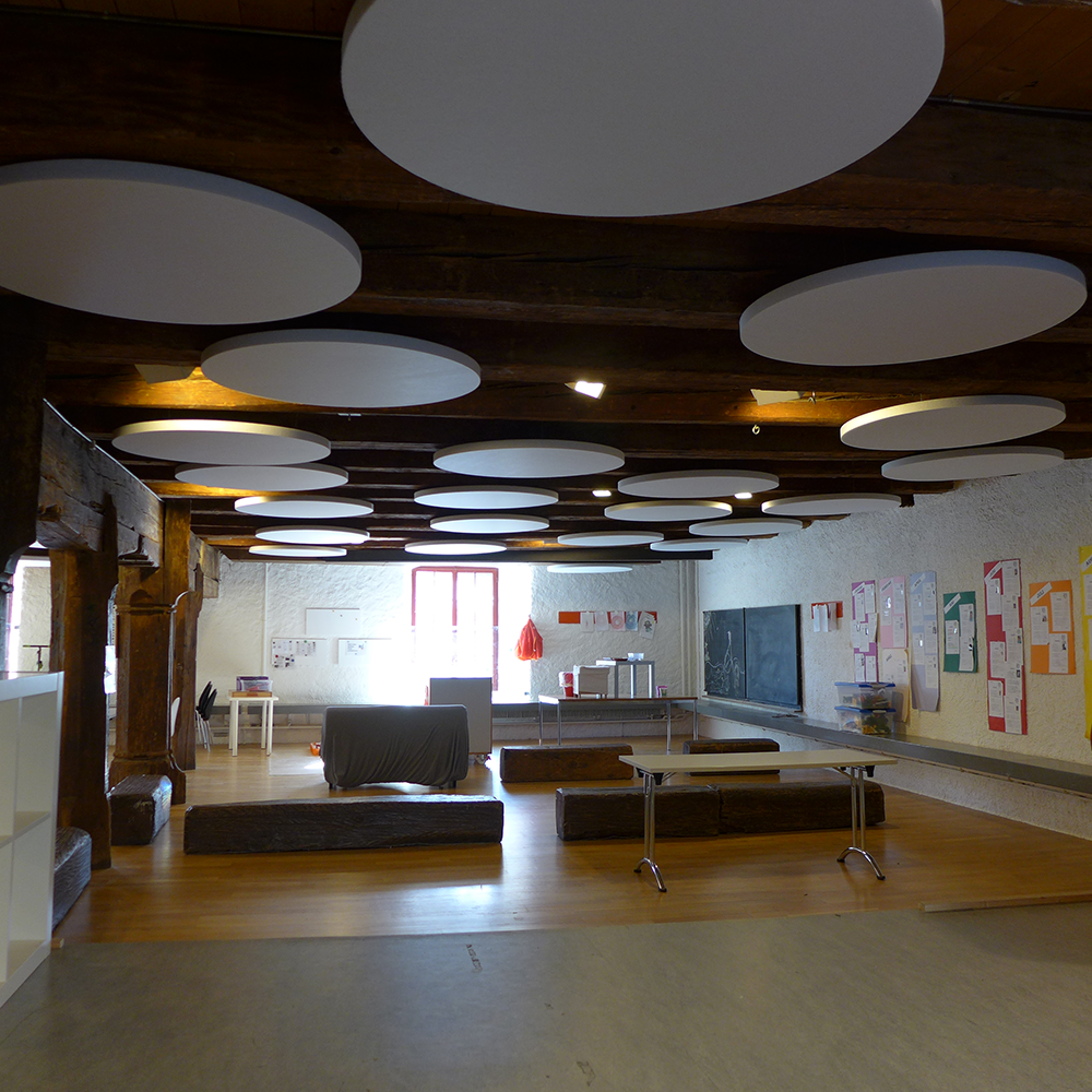 Ronde witte akoestische plafondpanelen onder een houten plafond in een loungeruimte