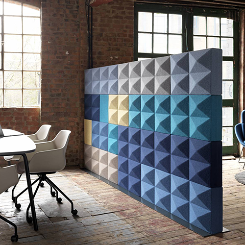 Akoestische wand van piramideblokken in grijs, blauw en geel als roomdivider in een loftruimte