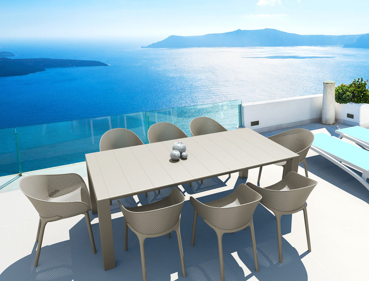 Sfeerbeeld van een lange lichte kantinetafel met beige stoelen op een terras aan zee
