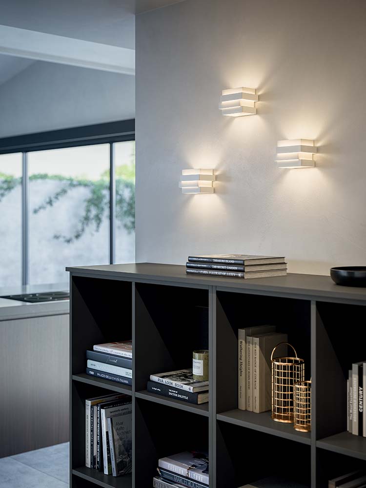 Witte wandlamp met gelaagde metalen banen tegen een lichte wand