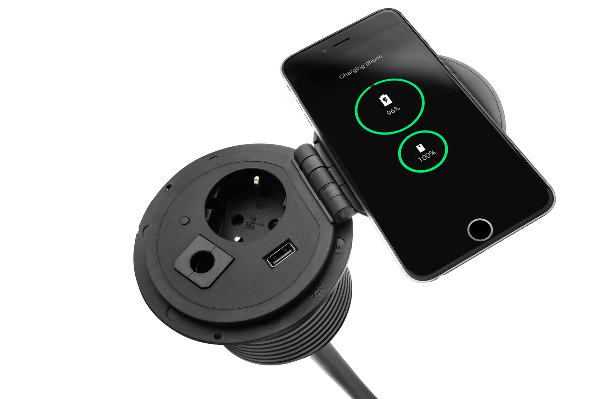 Ronde zwarte inbouwmodule met stopcontact en USB-poort, met een smartphone op de draadloze lader