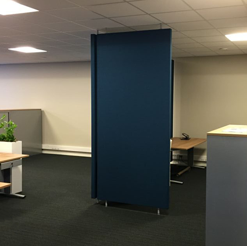Eén donkerblauwe roomdivider vrijstaand op donker tapijt, met bureaus en een plant erachter