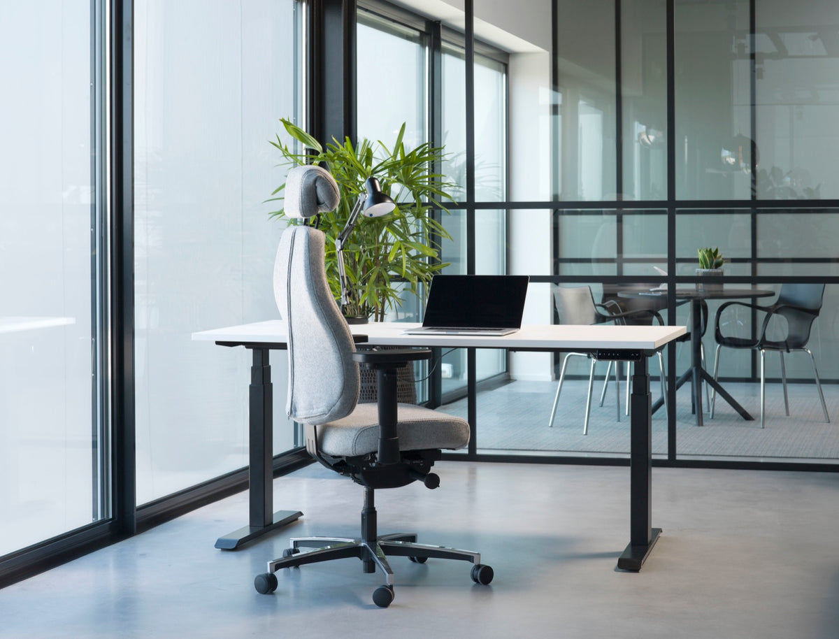 Sfeerbeeld van de stoel met hoofdsteun aan een licht zit-sta bureau in een kantoor met glaswanden