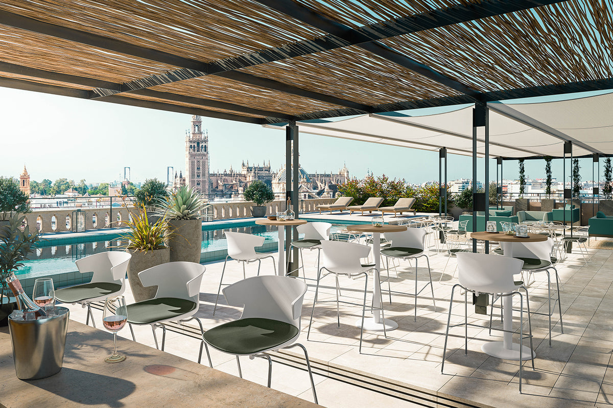 Sfeerbeeld van een dakterras met witte kuipstoelen en krukken bij ronde tafels onder een rieten pergola