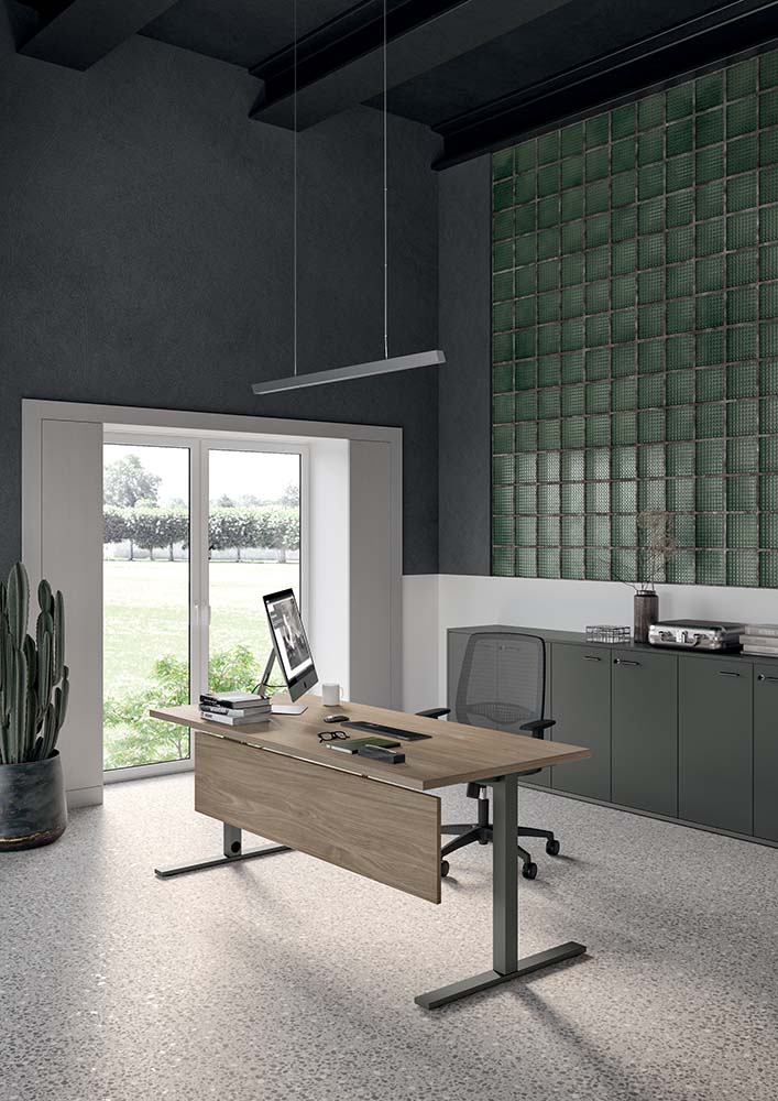 Sfeerbeeld van een donkere kantoorruimte met een bureau in houtdecor op zwarte poten bij een groene glaswand