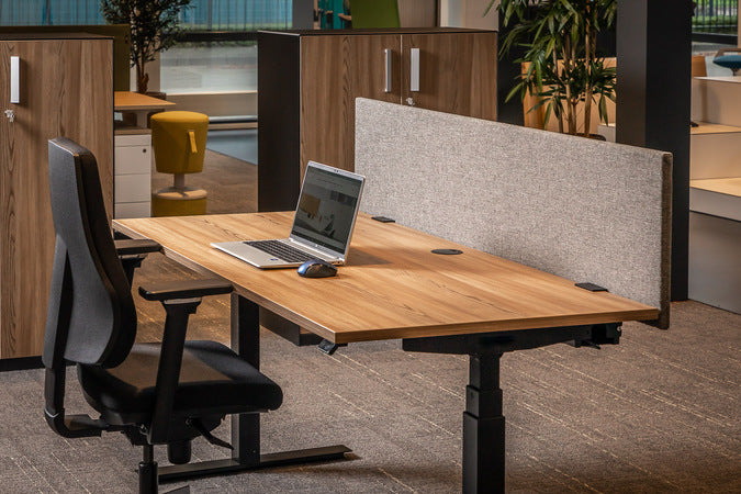 Het beige scherm op een zit-sta bureau met laptop, in een kantoor met houten kasten en een plant