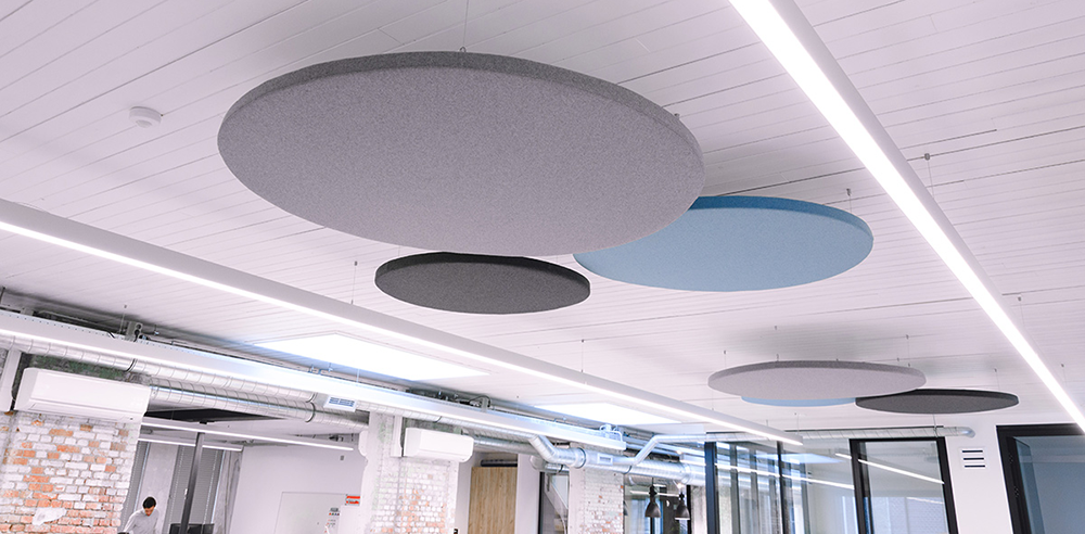 Grote ronde akoestische plafondpanelen in grijs en blauw onder een wit plafond met lichtlijnen