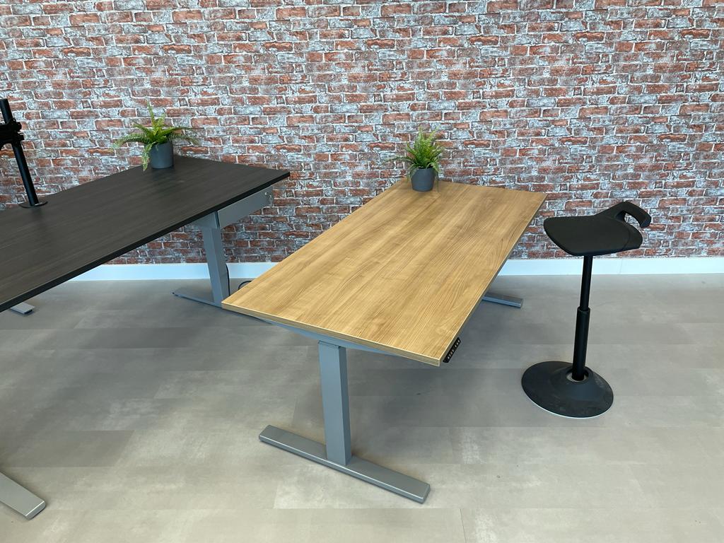 Elektrisch hoekbureau Ciao met grijs onderstel naast een statafel in de showroom