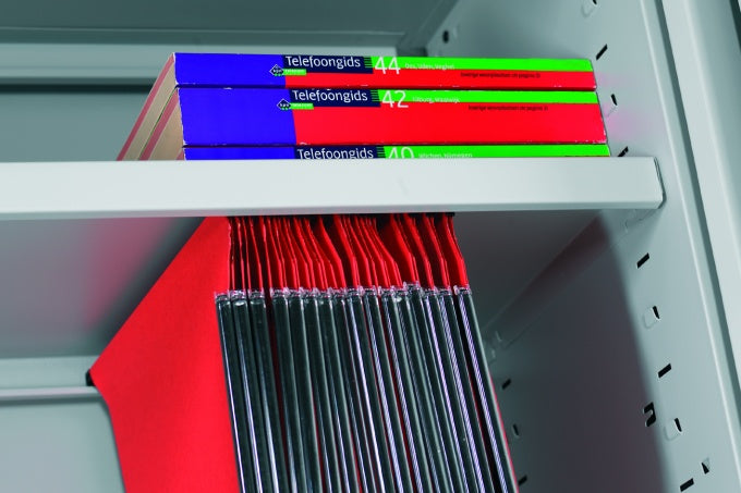 Lichtgrijs metalen legbord gemonteerd in een kast, met ordners erop en hangmappen eronder