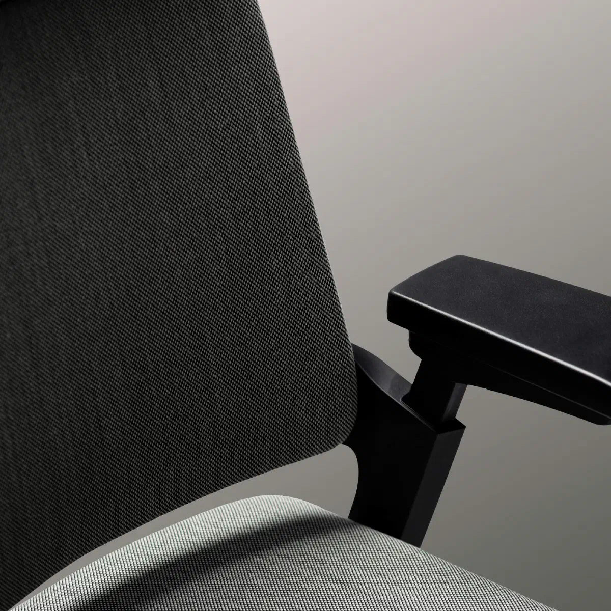 Detailopname van de zwart gestoffeerde rugleuning met armlegger boven een lichtgrijze zitting