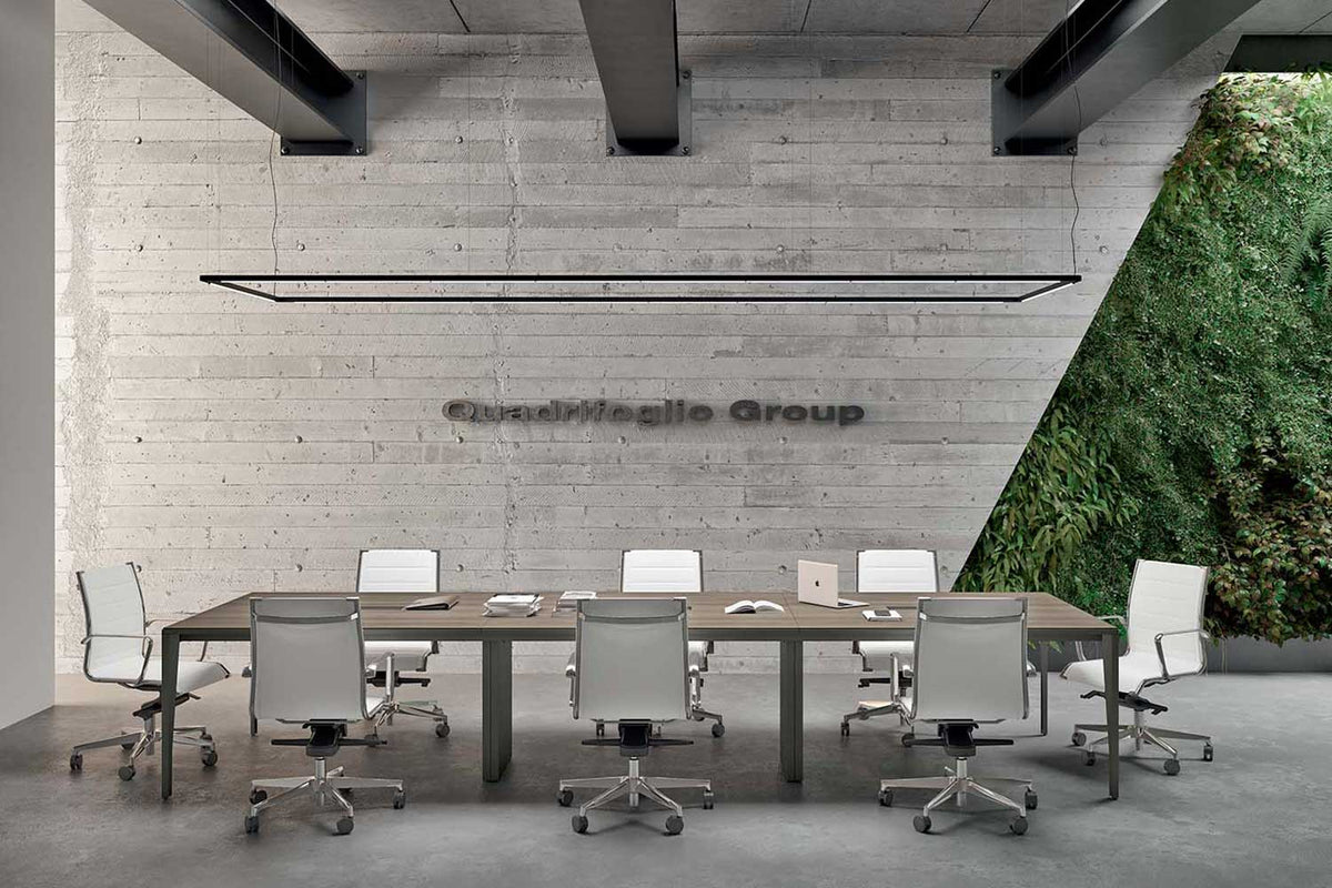 Lange vergadertafel met witte bureaustoelen in een ruimte met betonnen balken en een plantenwand