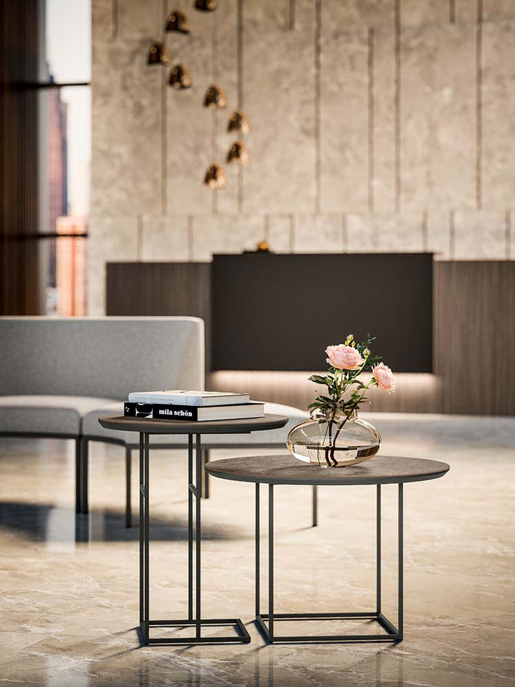 Twee ronde bijzettafels op zwarte metalen frames in een lounge, met bloemen en boeken erop