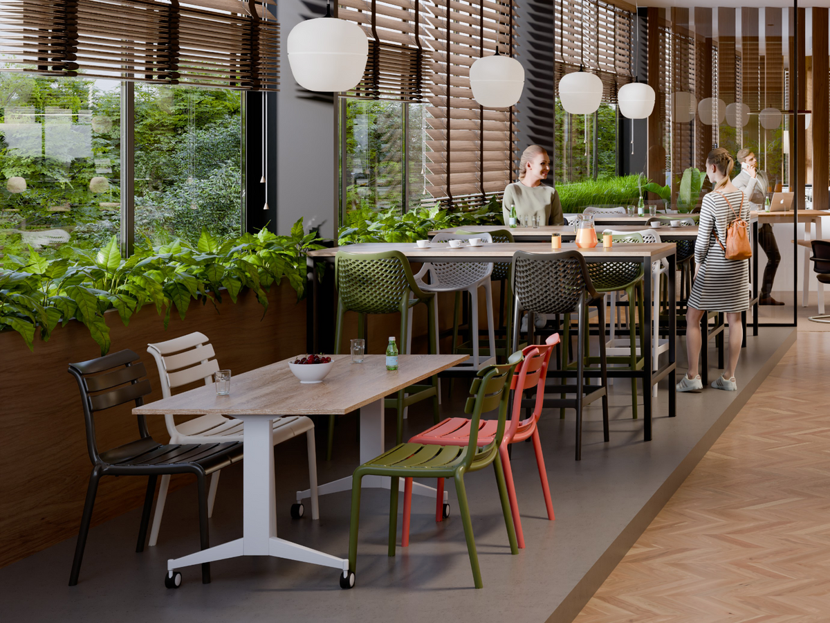 Sfeerbeeld van een horecaruimte met houten tafels en gekleurde stoelen langs een plantenwand